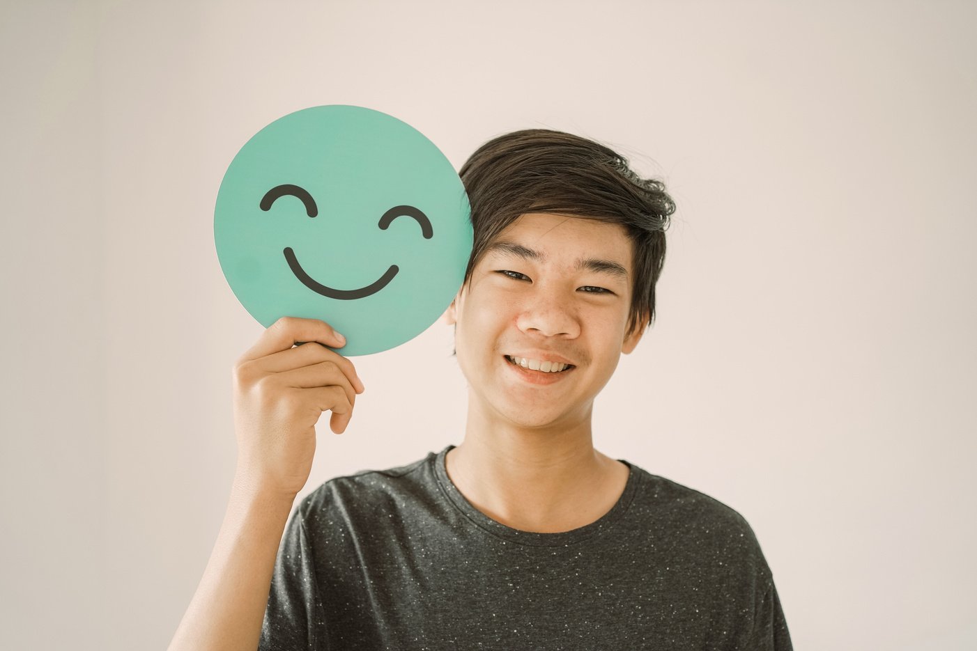 Happy mixed Asian teen boy holding smile emoji face, positive mental health concept